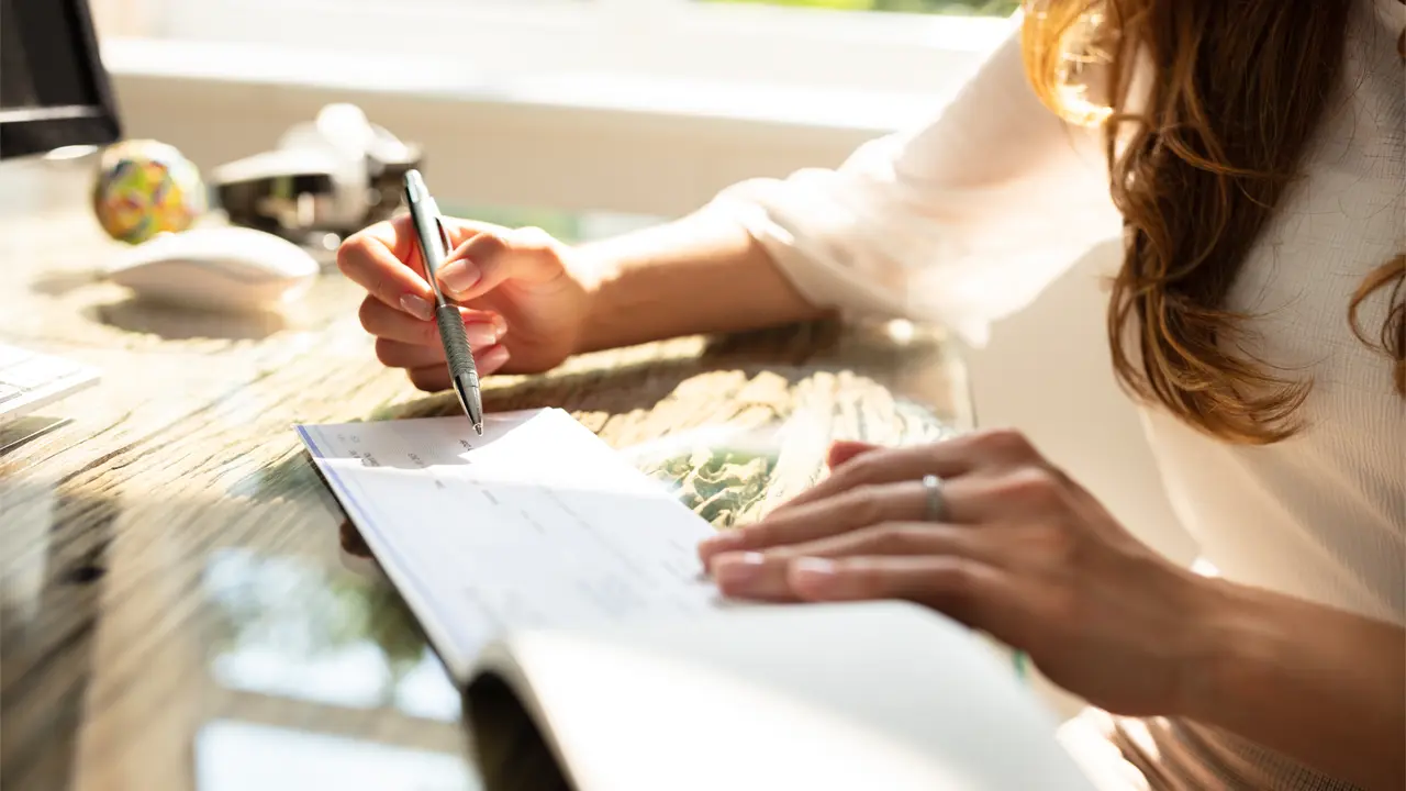 A close-up of a person writing or reviewing financial documents at a sunlit desk for responsible payment collections.